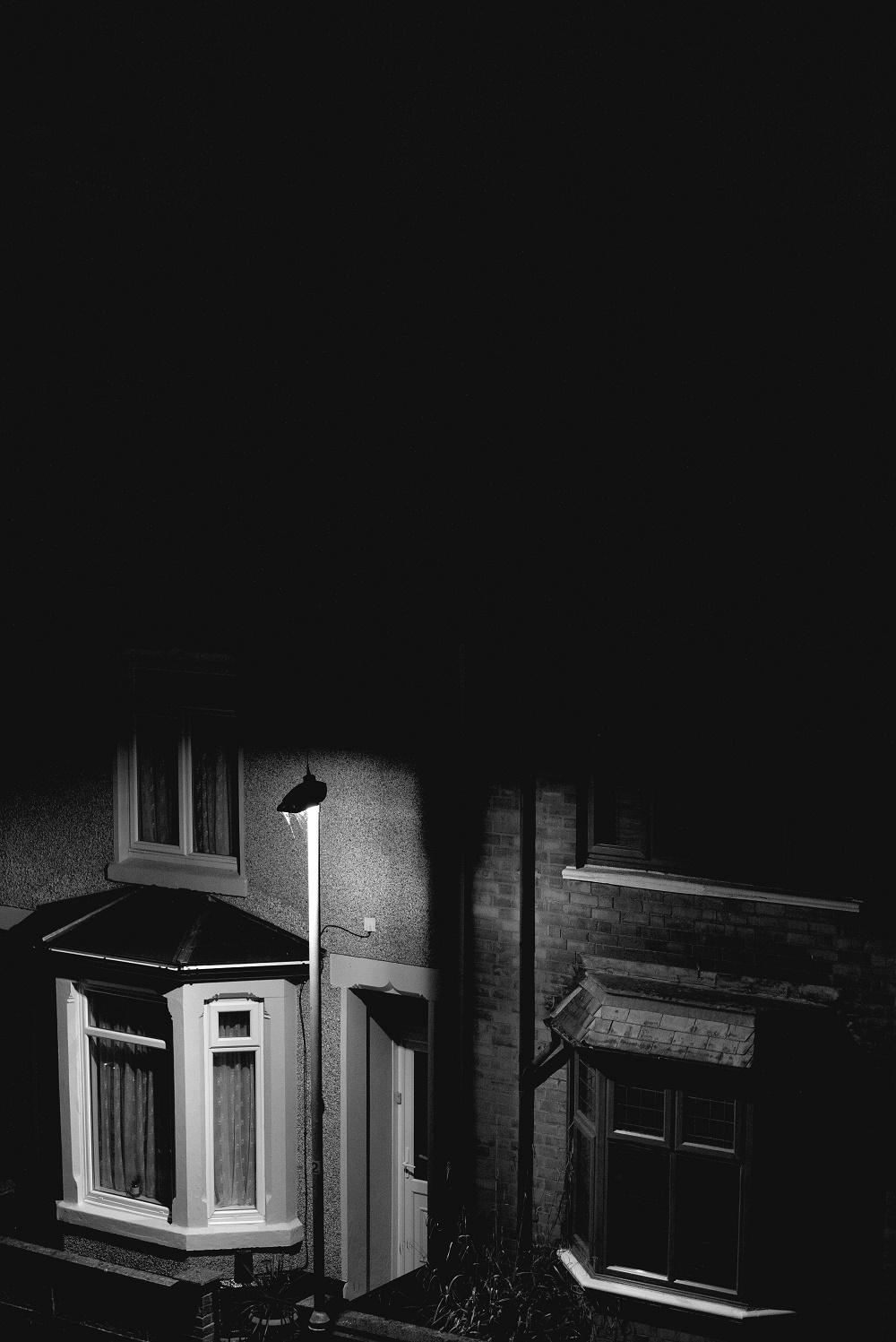 This black and white image shows a facade of a house at night.